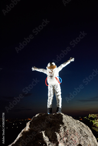 Back view of space traveler standing on top of rocky mountain and spreading hands in sides. Astronaut raising arms while looking at fantastic night sky. Concept of cosmonautics, space travel, freedom © anatoliy_gleb