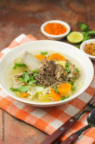 Sop Tulang Sapi or Indonesian clear beef soup mixed with some vegetables such as carrot, potato, cabbage, and green bean. Served on ceramic bowl , with sambal and onion crackers as condiments.
