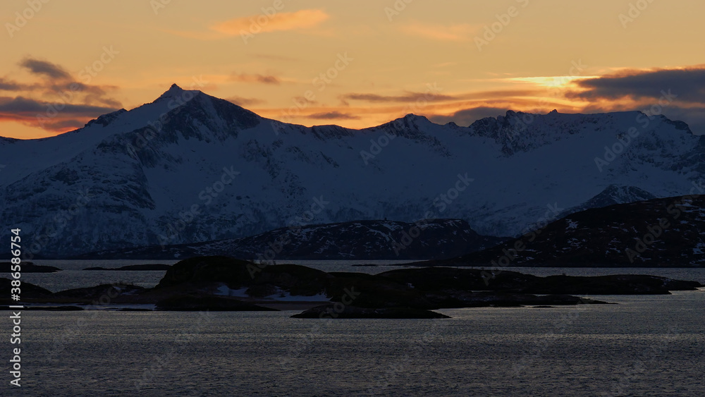 Stunning view of snow-covered craggy mountains at the shore of a fjord near Brensholmen, Norway, Scandinavia with beautiful colored sky during sunset in winter time. Stunning view of snow-covered craggy mountains at the shore of a fjord near Brensholmen, Norway, Scandinavia with beautiful colored sky during sunset in winter time.