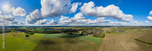Sunny panorama of rural idyll with fields, long lime tree avenue and village in the countryside. Magical farmland landscape in autumn.