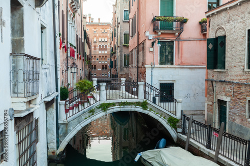 Bridge across narrow water canal in Venice between old buildings with balconies and brick walls. Italy. © alexxich