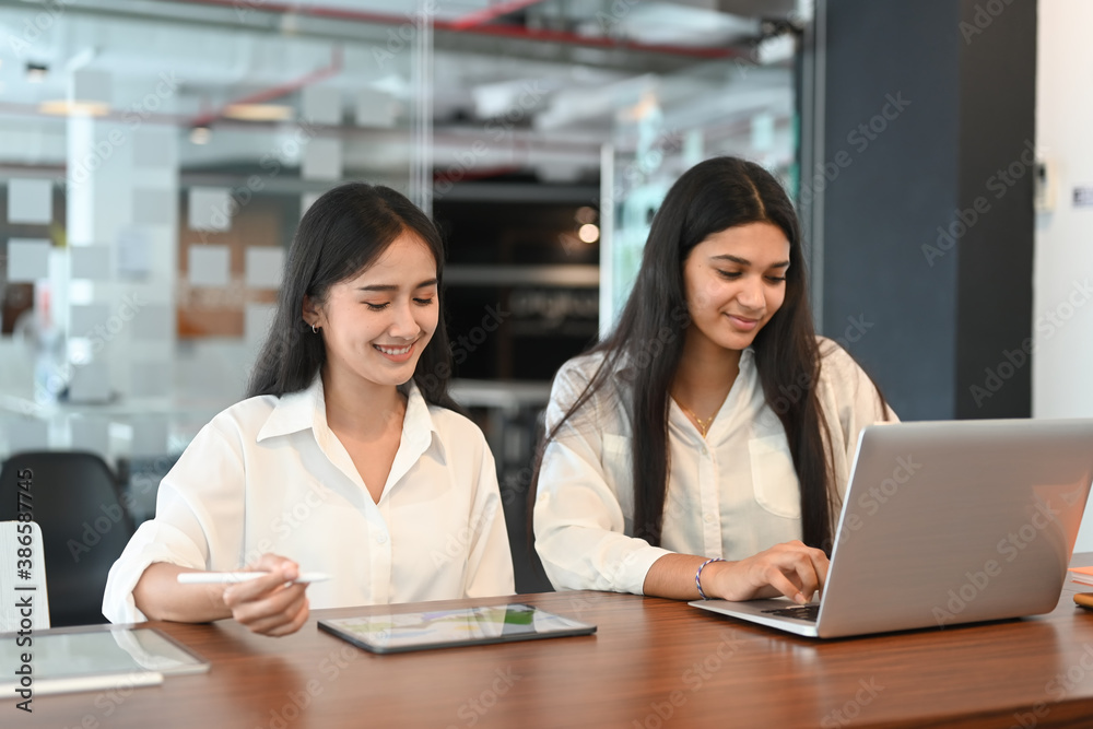 A diverse team of two coworkers working over a laptop at modern office. A diverse team of two coworkers working over a laptop at modern office.