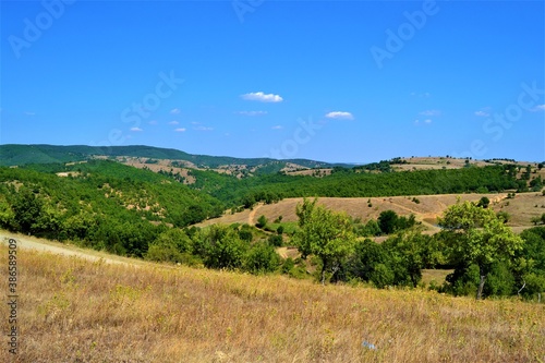 Bulgaria and views from cute and small villages during bright day. Natural land with yellow grass and blue sky and cute white cloud.