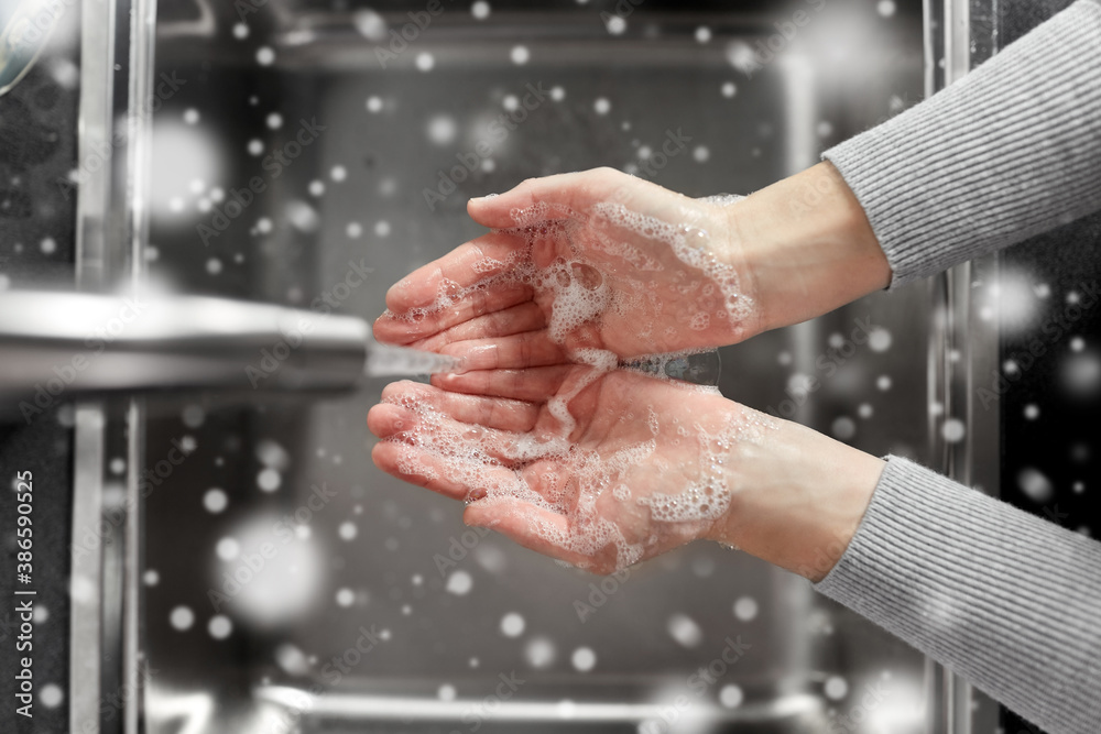 hygiene, health care and safety concept - close up of woman washing hands with soap and water in kitchen at home in winter over snow