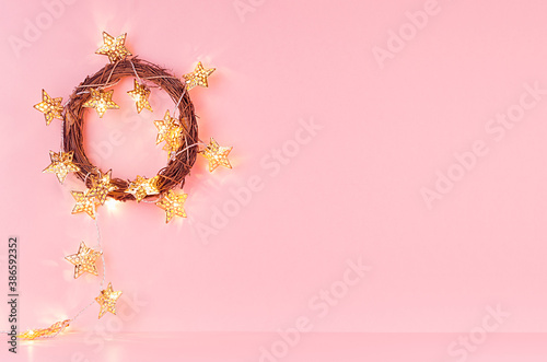 Christmas wreath with gold shimmer glowing stars garland on soft light pastel pink background, copy space, interior.