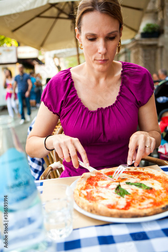 Urban portrait of a dark haired woman eating pizza outdoors.