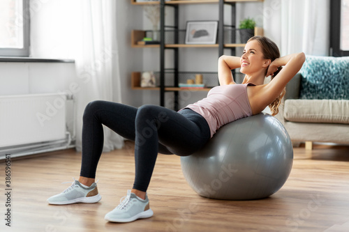 sport and healthy lifestyle concept - happy woman exercising on fitness ball at home