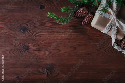 On a wooden, brown background lies a box with a gift, a sprig of a Christmas tree and cones. photo
