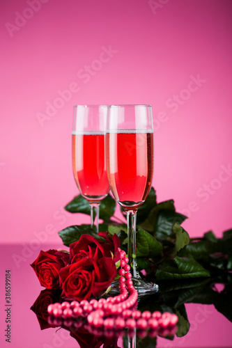 Studio photo of pink champagne with red roses on pink background and reflective surface.