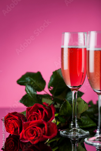 Studio photo of pink champagne with red roses on pink background and reflective surface.