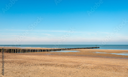Empty North Sea sand beach on a sunny winter day. Breakwaters of wooden posts are clearly visible because of low tide. The photo was taken near the Dutch village of Domburg, Walcheren, Zeeland.