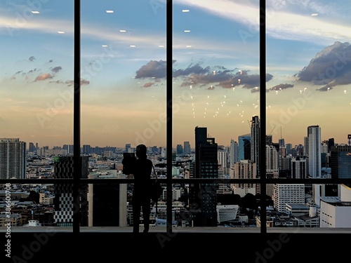 silhouette outline of women tourist taking pictures of city skyline from an observatory. sunset at modern urban business district. steel frame rose windows architectural element design.