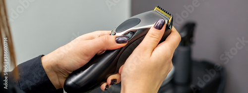 Hair clipper in hands of female professional hairdresser or barber in hair salon