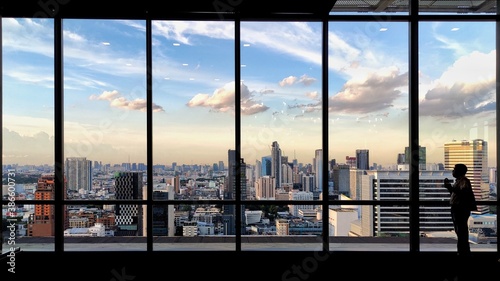 silhouette outline of women tourist taking pictures of city skyline from an observatory. sunset at modern urban business district. steel frame rose windows architectural element design.