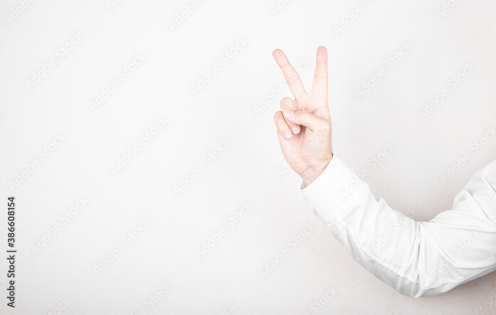 Man hand shows victory gesture, point number two on white wall background Man hand shows victory gesture, point number two on white wall background