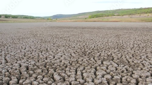 A huge area of a very dry lake suffering from drought, next to it everything is green. The soil is very dry and cracked photo