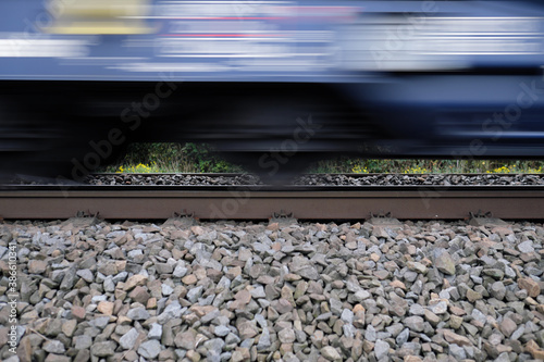 Gleisbett mit Schotter und Gleis und Ausschnitt von vorbeifahrendem Güterzug mit Bewegungsunschärfe - Stockfoto