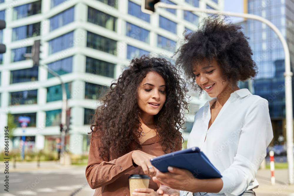  Two businesswomen checking something on the tablet in the city