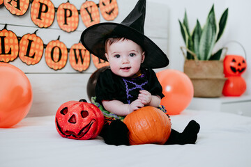 beautiful baby girl in witch halloween costume at home, sitting on bed with Halloween decoration, Lifestyle indoors
