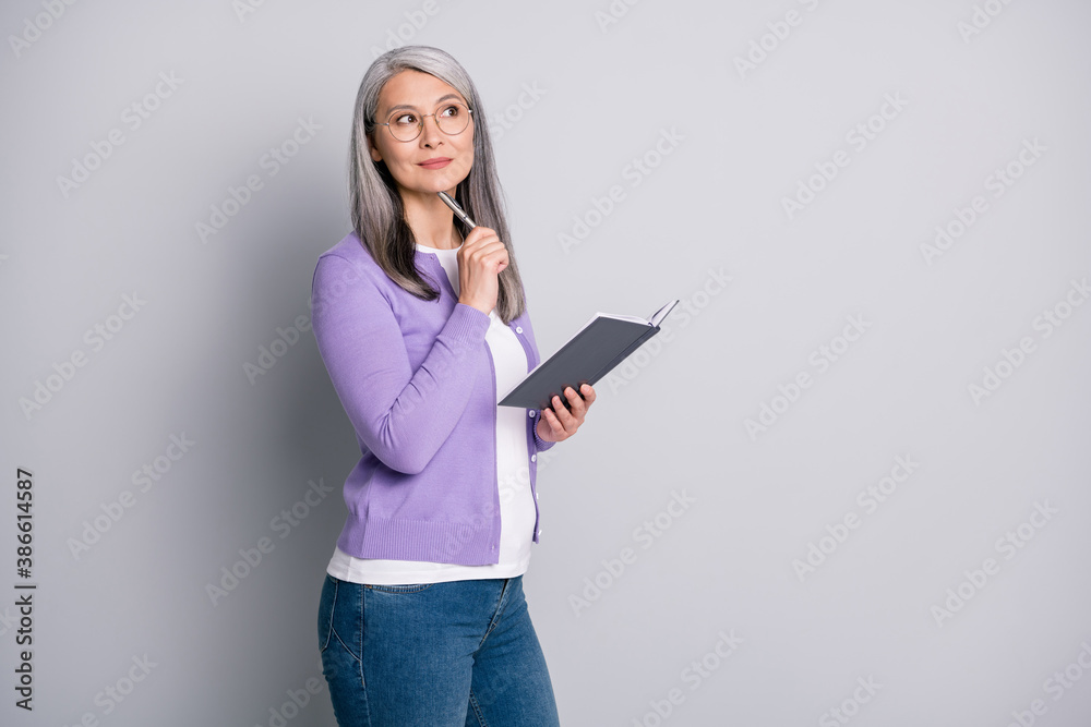 Photo portrait of senior businesswoman writing notes new idea in planner with a pen dreaming isolated on grey color background with blank space Photo portrait of senior businesswoman writing notes new idea in planner with a pen dreaming isolated on grey color background with blank space