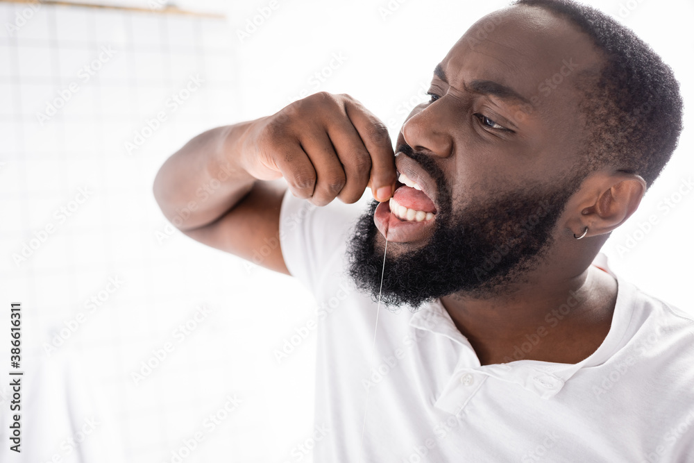 Fototapeta premium afro-american man using dental floss in bathroom