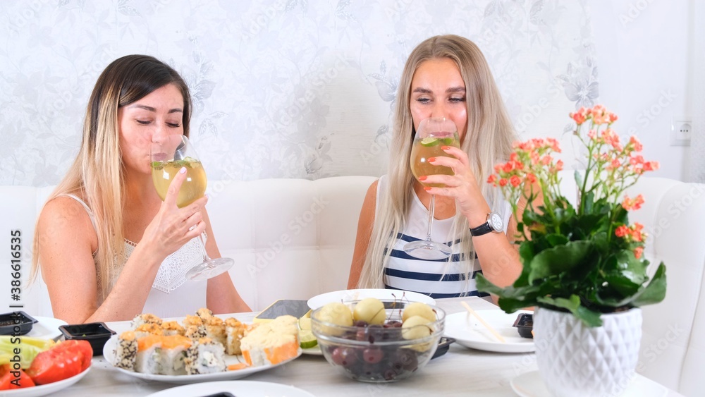 Two attractive girls, best friends are sad and drink wine at home. Two glasses of white wine in hand.