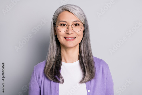 Portrait photo of positive smiling elder woman wearing eyeglasses and purple cardigan isolated on grey color background
