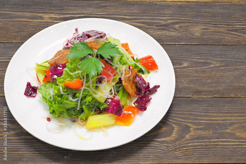 Chinese cuisine. Cabbage salad with celery and starch noodles on a white plate on a wooden table. Chinese cuisine. Cabbage salad with celery and starch noodles on a white plate on a wooden table.