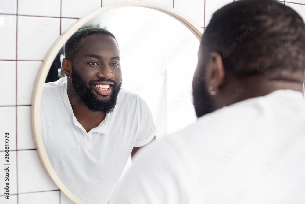 smiling afro-american man looking in mirror - obrazy, fototapety, plakaty 