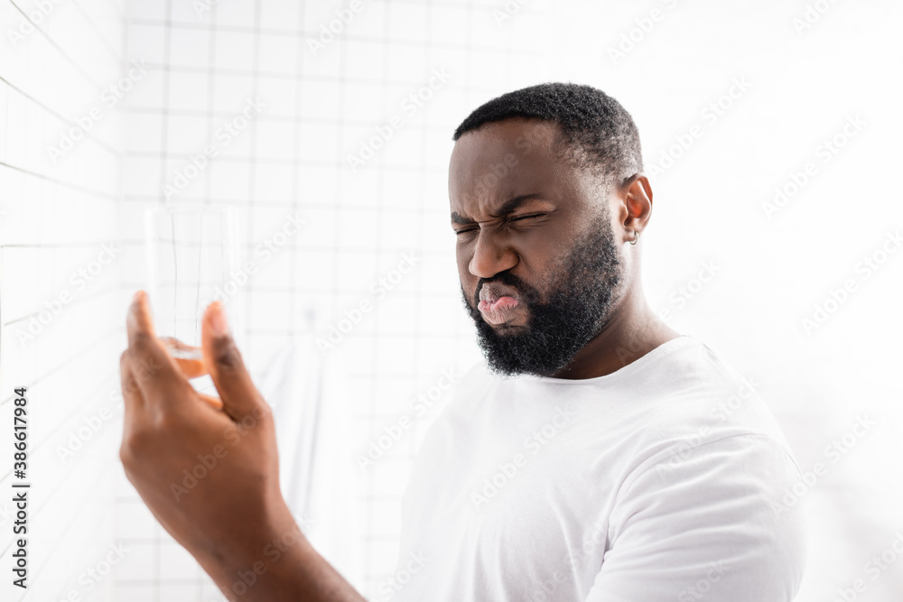 afro-american man grimacing from bad taste of water and holding glass in hand - obrazy, fototapety, plakaty 