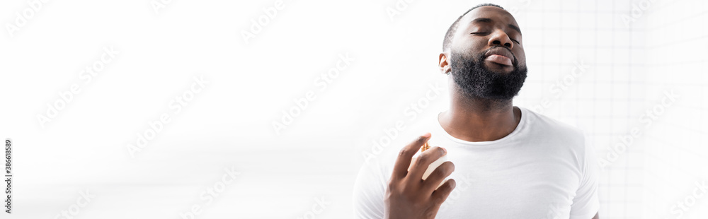 Obraz premium panoramic shot of afro-american man in white t-shirt using perfume