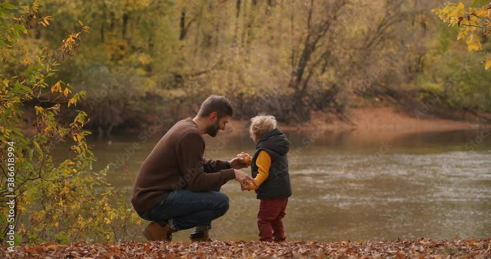 happy father is talking with his child son in forest, standing on coast of lake or river at autumn weekend, family trip happy father is talking with his child son in forest, standing on coast of lake or river at autumn weekend, family trip