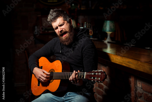 Handsome bearded man playing guitar at the pub. Talented romantic person singing song.