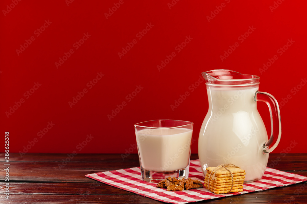 Glass pitcher and cup of milk against red background Glass pitcher and cup of milk against red background