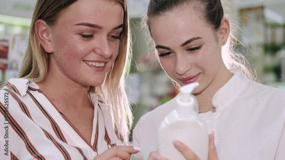 A drug store worker is helping a female client to choose right medicine. The pharmacist woman and the client are standing near the trade shelf. A drug store worker is helping a female client to choose right medicine. The pharmacist woman and the client are standing near the trade shelf.