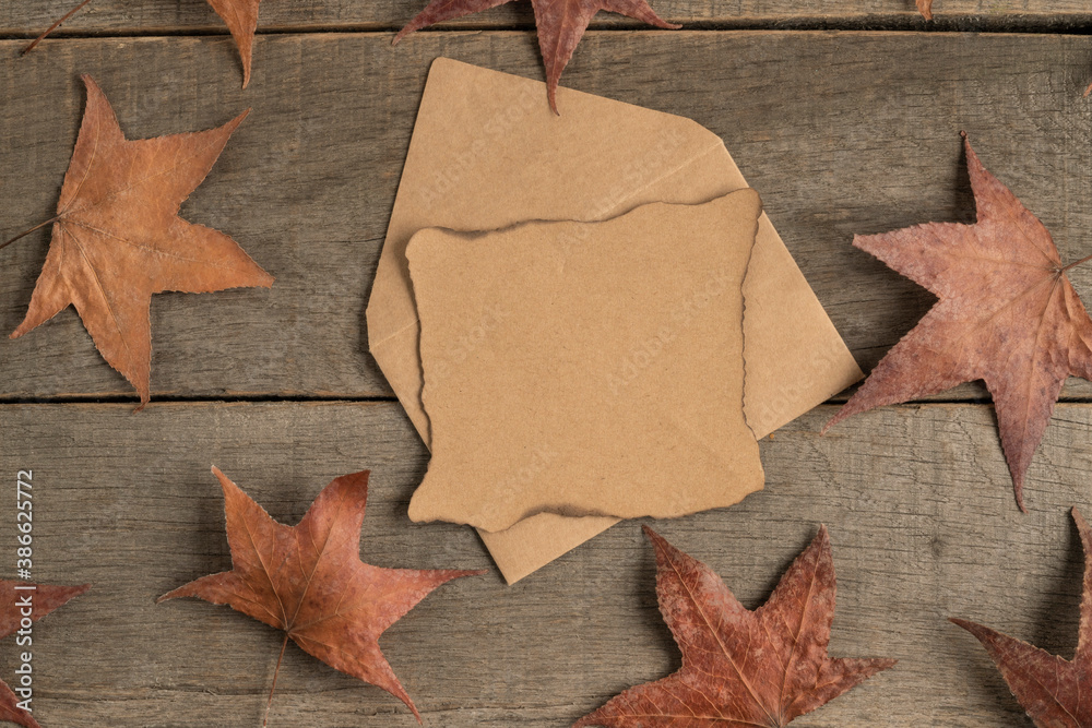 blank paper and envelope on wooden table decorated with dried autumn leaves