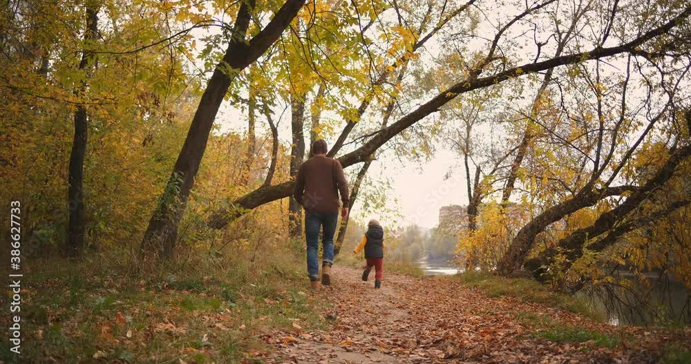 running father and little son in autumn forest, back view of figures, having fun at weekend walks at nature running father and little son in autumn forest, back view of figures, having fun at weekend walks at nature
