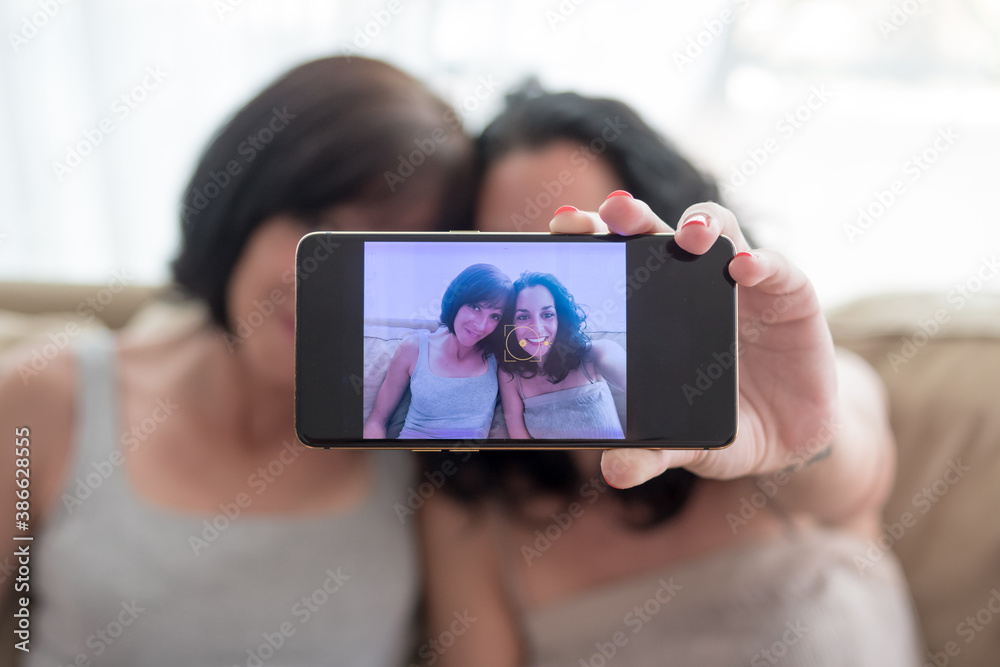 two young women have fun and laugh while taking a selfie with their phones