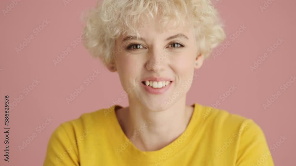 A close-up view of a positive blonde young woman is sending air kiss to the camera standing isolated over pink background A close-up view of a positive blonde young woman is sending air kiss to the camera standing isolated over pink background