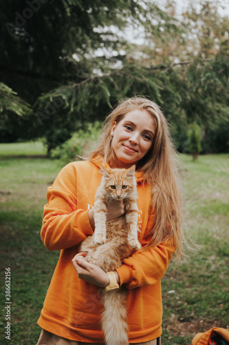 Young Caucasian girl holding a red cat in her hands. Autumn concept. Having a pet concept.
