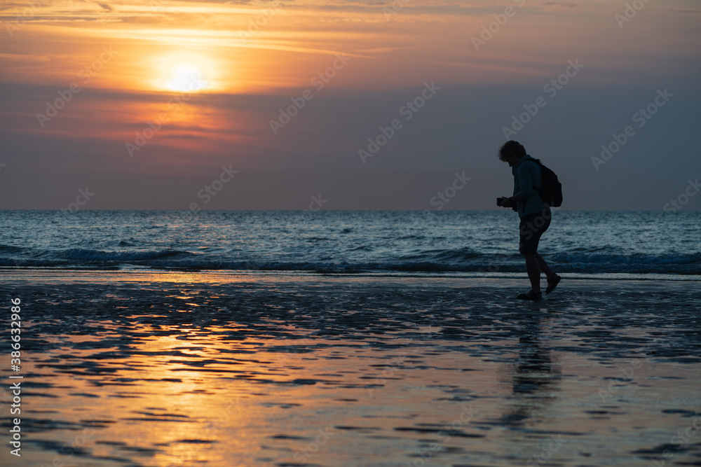 A woman walks by the beach in a a profusion of colors at sunset.