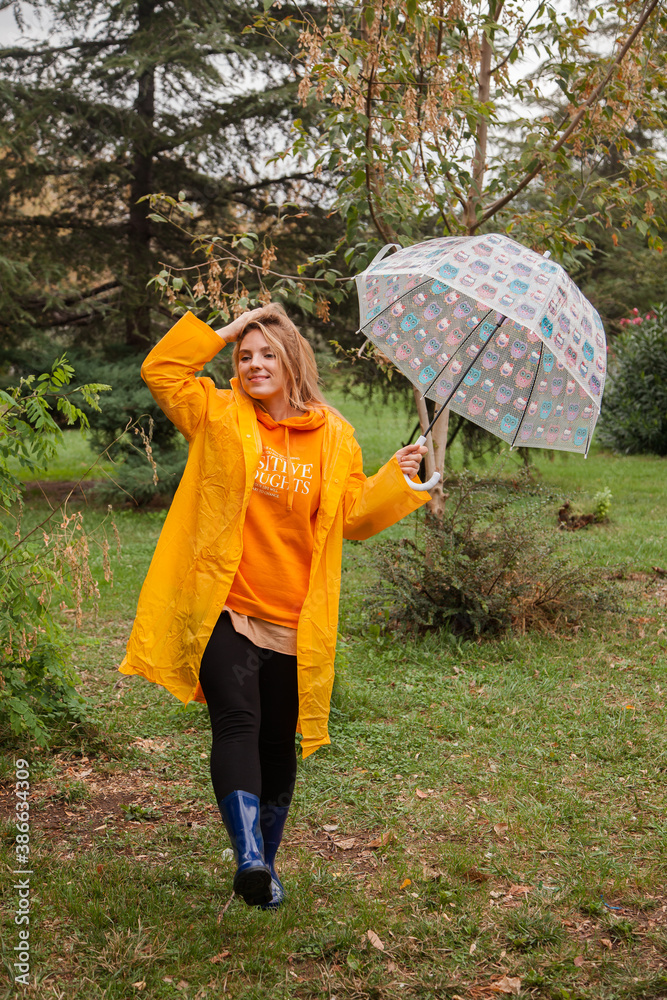 Caucasian girl in a yellow raincoat walking outside in the rainy day in autumn. People in fall