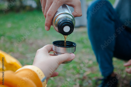 Hand holding a thermos with coffee, drinking coffee outdoors. Trekking concept. 