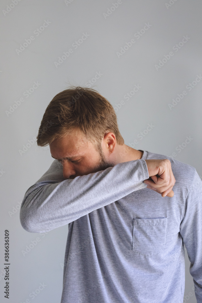 Man sneezing on his elbow against grey background Man sneezing on his elbow against grey background