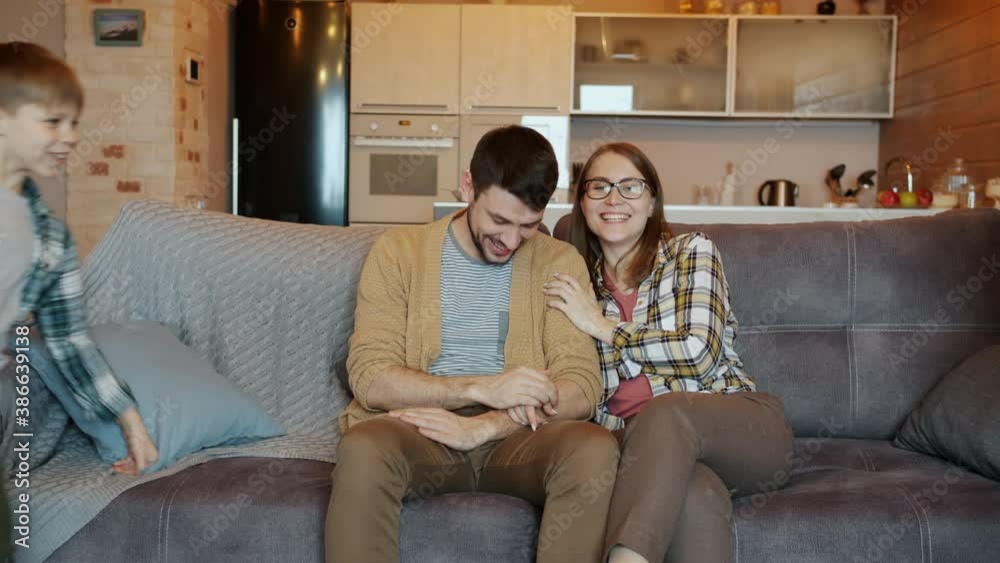 Portrait of happy young couple man and pregnant woman watching TV and talking when kids are coming hugging laughing relaxing on couch at home Portrait of happy young couple man and pregnant woman watching TV and talking when kids are coming hugging laughing relaxing on couch at home