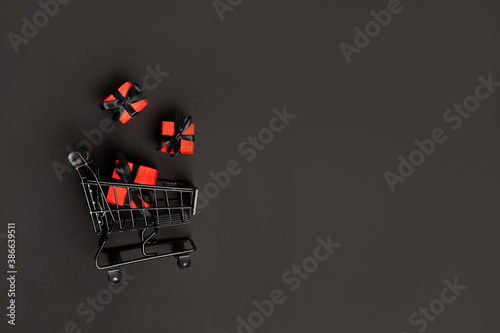 red paper bags in shopping cart on black background, copy space. black friday concept
