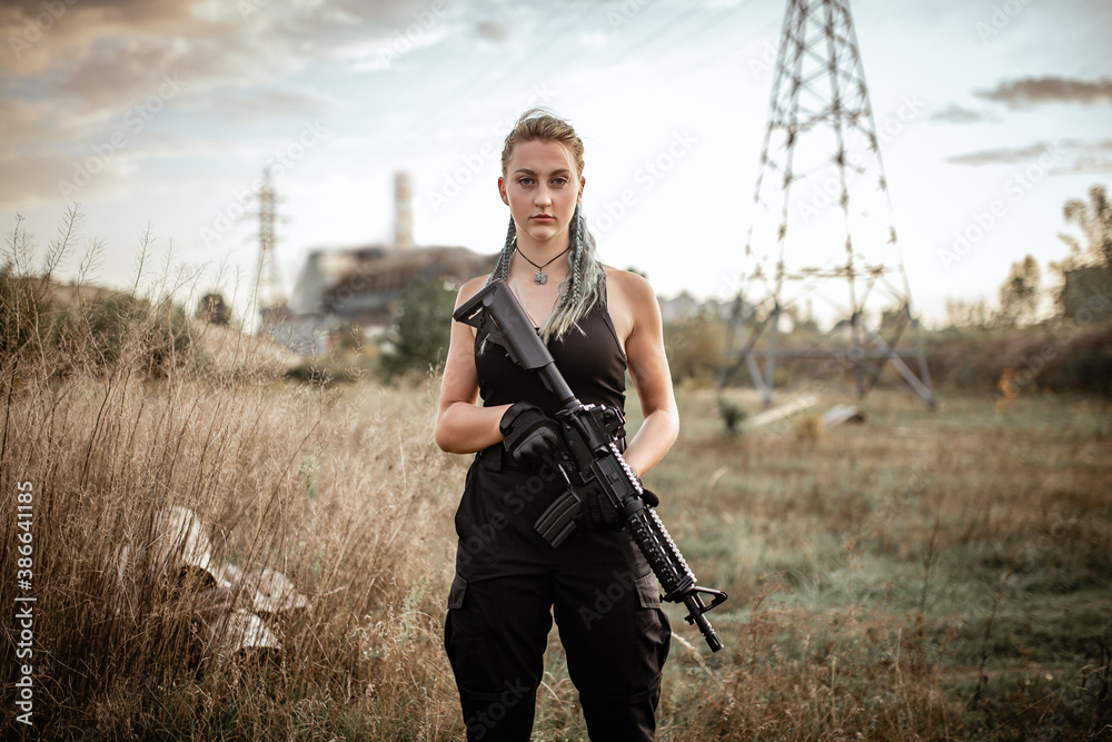 Fototapeta premium Sexy woman posing with a rifle outdoors on the background of the Chernobyl sarcophagus