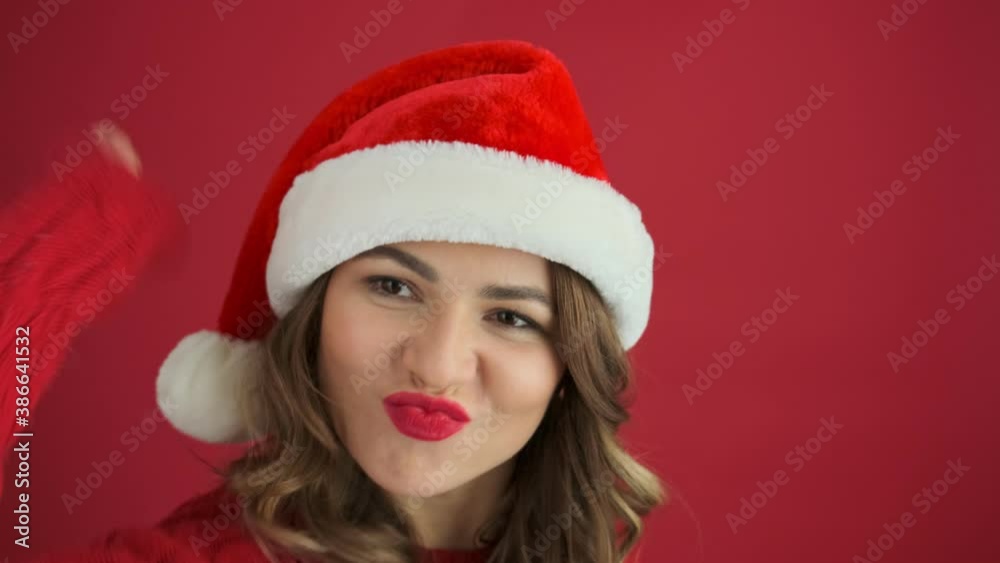 An angry woman wearing a warm red sweater and christmas hat is knocking on the door standing isolated over red background