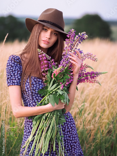 Obraz na płótnie Girl with lupins in a lilac dress and a hat in a wheat field w salonie