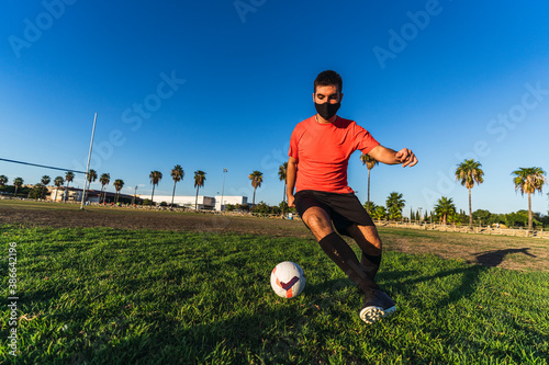 Chico joven con mascarilla por el covid 19 preparandose y jugando al futbol